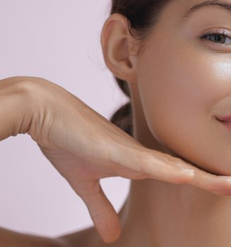 Junge Frau präsentiert ihr Glow-Make-up mit der rechten Hand unter dem Kinn.